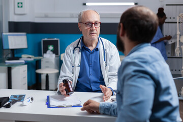 Fototapeta premium Physician showing bottle of pills to young man at consultation appointment, giving jar with medicine to cure illness. General practitioner holding healthcare treatment for patient.