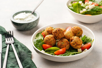 Salad bowl with chickpea falafel, fresh green spinach, cherry tomatoes, croutons and mint yoghurt dressing on a grey stone surface