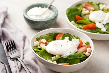 Salad bowl with fresh green spinach, cherry tomatoes, croutons, egg benedict and sour cream dressing on a grey stone surface