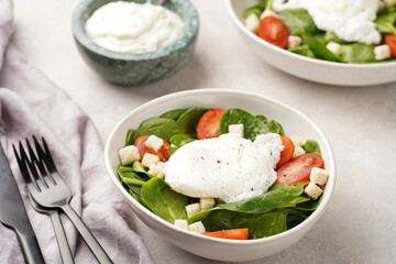 Salad bowl with fresh green spinach, cherry tomatoes, croutons, egg benedict and sour cream dressing on a grey stone surface