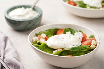 Salad bowl with fresh green spinach, cherry tomatoes, croutons, egg benedict and sour cream dressing on a grey stone surface