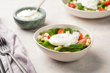 Salad bowl with fresh green spinach, cherry tomatoes, croutons, egg benedict and sour cream dressing on a grey stone surface