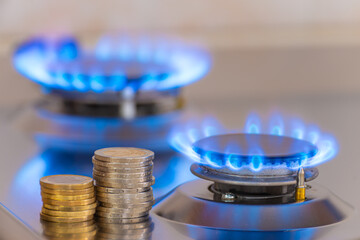 Gas stove lit, with stacks of coins above it. Increase in gas costs and tariffs.
 - obrazy, fototapety, plakaty
