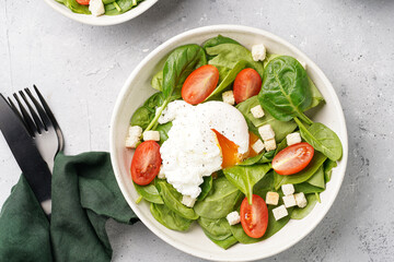 Salad bowl with fresh green spinach, cherry tomatoes, croutons, egg benedict and sour cream dressing on a grey stone surface