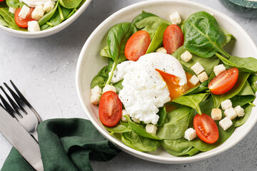 Salad bowl with fresh green spinach, cherry tomatoes, croutons, egg benedict and sour cream dressing on a grey stone surface