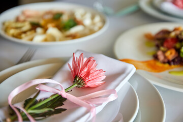 Obraz na płótnie Canvas Cloth napkin with pink chrysanthemum lie on a plate in a restaurant. Close-up, selective focus