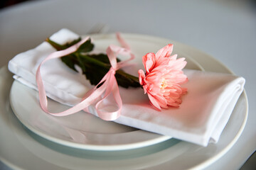 Cloth napkin with pink chrysanthemum lie on a plate in a restaurant. Close-up, selective focus