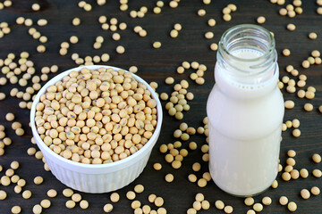 Bowl of Dried Soybeans and a Bottle of Soy Milk with Scattered Beans on Black Wooden Table 