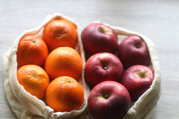 Two sustainable shopping bags filled with apples and oranges on wooden table. Selective focus.