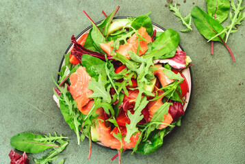 Fresh salmon salad with avocado, beet leaves, radicchio, tomatoes, lemon and olive oil dressing for keto and low carb diet. Rusty green background, top view, copy space