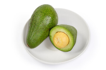 Whole and half of green avocado fruits on a saucer