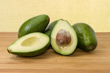 Whole and halved green avocado fruits on a wooden surface