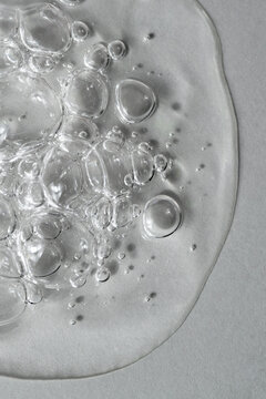 Transparent facial serum with bubbles on light grey background macro. Liquid bubbly gel with hyaluronic acid closeup. Moisturising cosmetic product texture. Beauty and spa concept. Top view.
