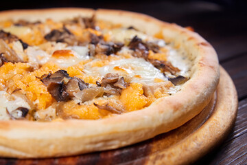 Pizza with cheese and mushrooms on a wooden plate. Close-up, selective focus