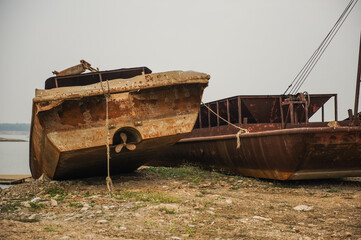 Abandoned rusty dredgers parked along riverbanks.