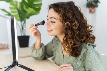pretty woman with curly hair putting on makeup at home with a brush - Powered by Adobe