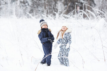 Fototapeta na wymiar Happy Children playing outdoors in cold winter weather, having fun and throwing snow in the forest. Active holidays