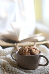 Bowl of chocolate chip cookies, soft knitted basket, wicker basket and candle holder with lit candle. Hygge at home. Selective focus.