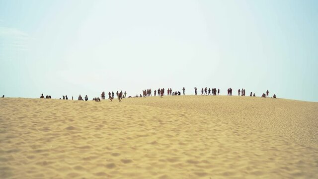 Duna de arena con siluetas de mucha gente en la parte superior 