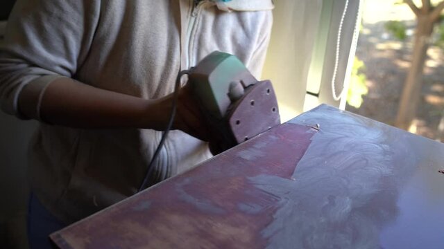 Chica joven guapa con mascarilla lijando un mueble para restaurarlo 