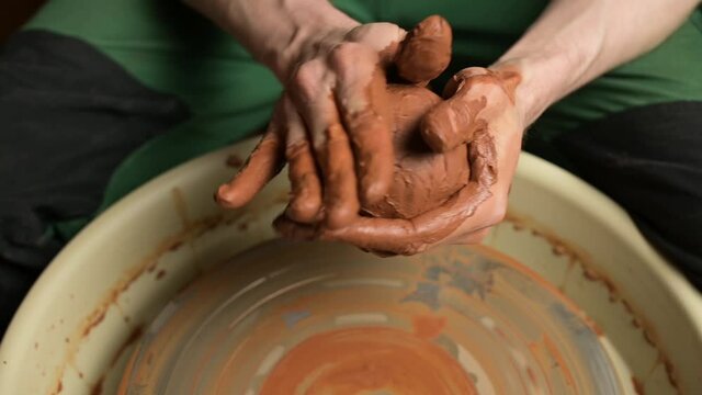 The hands of a master crumple brown clay in preparation for the production of a clay pot