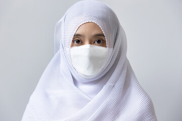Muslim woman in white dress and headscarf wearing face mask