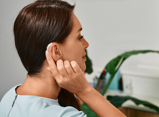 Adult woman with hearing aid behind the ear can hear sounds. Hearing loss treatment concept and...