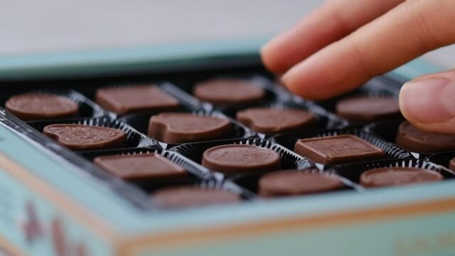 Woman take one chocolate from a box of different candies. Close-up shooting stock footage. slow motion