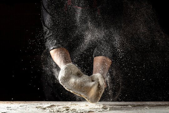 Beautiful and strong men's hands knead the dough make bread, pasta or pizza. Powdery flour flying into air. chef hands with flour in a freeze motion of a cloud of flour midair