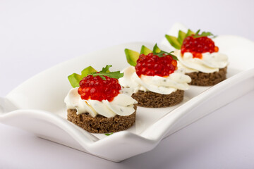 Sophisticated gourmet appetizers featuring rye bread, creamy spread, vibrant red caviar, and crisp avocado slices on a sleek white dish.