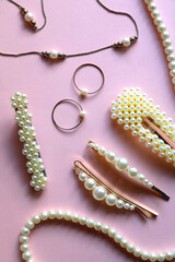 Various pearl jewelry and hair accessories on pink background. Flat lay.
