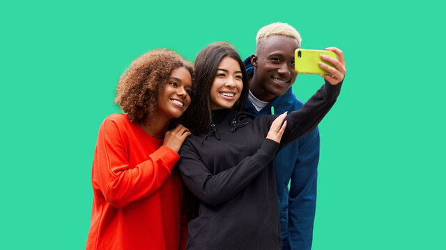 Studio shot of nice young multicultural friends. Beautiful people cheerfully smiling and having fun while making selfie photo. Isolated green background
