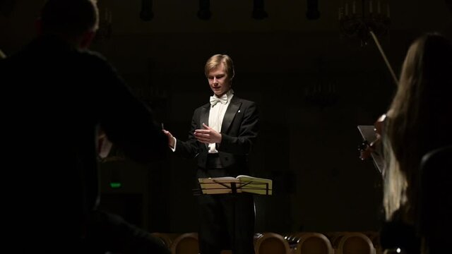 The camera zooms in on the conductor while the symphony orchestra is playing. Slow motion