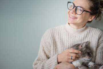 Young cheerful curly girl woman in eyeglasses holding a beautiful gray fluffy cat in her arms