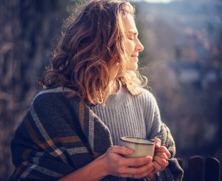Portrait of relaxed beautiful curly young woman enjoying morning coffee and nature on the balcony with forest view