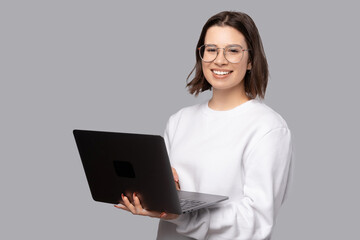Portrait of young smiling woman in white sweater holding laptop and looking at the camera.