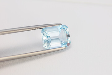 Light blue aquamarine gemstone in tweezer. Octagon shaped, emerald cut, transparent, with small...