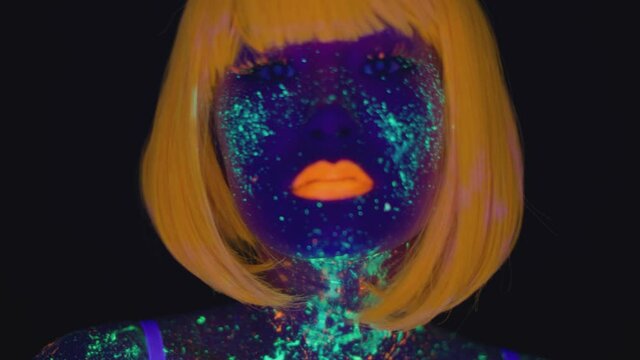 Young asian woman wearing orange wig with fluorescent makeup coming to camera and dancing over black background