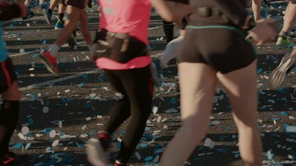 Starting line of urban city marathon. Crowd of participants run past camera towards finish. Healthy athletic running event. Paper confetti on floor. Marathon runners in Barcelona