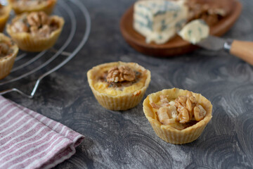 Tartlets with pear, blue cheese and walnut on a gray table, blue cheese on a wooden plate with a cheese knife, tartlets on the grate, striped napkin