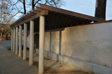 Fototapeta na wymiar wooden structure of the pergola supported by smooth cylindrical white columns shelter of a gazebo pergola. roof lined with glass. connects to the retaining wall with a brick roof