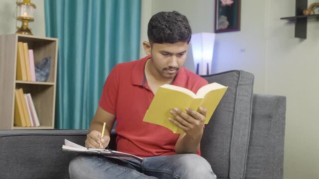 Young indin aspirant student noting or highlighting important lines while studying note books at home - concept of making study easier, learning and knowledge development.