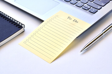Paper note to do list on laptop with pen and black book.