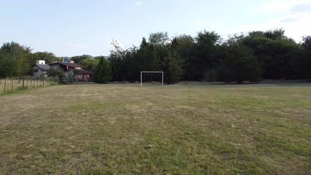 Empty soccer field. Approach to soccer goal. Green soccer field without players. Image from drone. Filming from the air. Concept of effort, road, travel, sports.