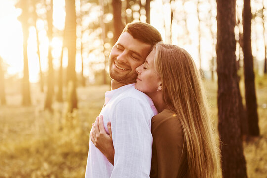 Illuminated by sunlight. Happy couple is outdoors in the forest at daytime