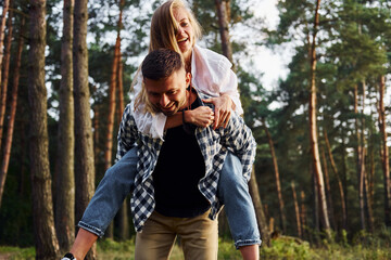 Woman is riding her man. Happy couple is outdoors in the forest at daytime