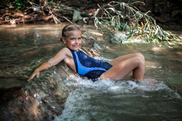 Happy girl swimming under waterfall in stream canyon river in the mountains, nature pool. Cold water, hardening and natural spa procedure, wildlife and green tourism, summer holidays
