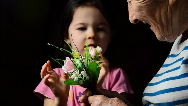 The granddaughter gives her grandmother flowers. Mothers Day. Giving flowers to grandmother. Two generations of women. The child gives flowers to his grandmother. Flowers in wrinkled hands. 