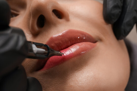Young woman undergoing procedure of permanent lip makeup in tattoo salon, closeup