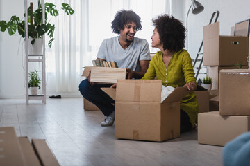 Happy playful African American couple moving in a new apartment, unpacking, moving stuff, purchase...